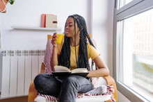 Calm Black Woman With Book Drinking Orange Juice