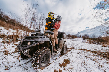 Couple enjoying while driving quad bike on top of mountain at winter time