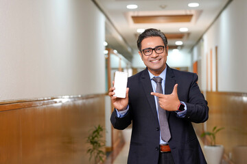 Young businessman showing smartphone screen on office background