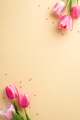 Wall Mural - Mother's Day celebration concept. Top view vertical photo of bunches of pink tulips and heart shaped sprinkles on isolated pastel beige background with copyspace