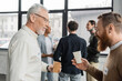 © LIGHTFIELD STUDIOS - Smiling men with paper cups talking during alcoholics meeting in recovery center.