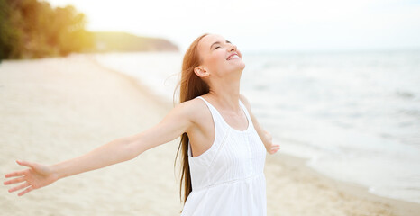 Happy smiling woman in free happiness bliss on ocean beach standing with open hands. Portrait of a multicultural female model in white summer dress enjoying nature during travel holidays vacation