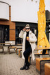 © DSMT - A young pretty woman in a white fur coat and sunglasses with coffee walks around the city. Stylish young girl.