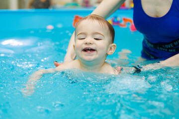 Wall Mural - A 2-year-old little boy learns to swim in a pool with a coach. Swimming lessons for children