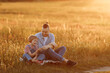 © Kaplitskaya Love - A touching moment, captured in time, when a little girl in denim overalls sits with her father in the field, they enjoy a walk in the field on a summer evening.