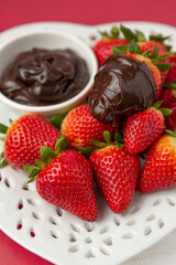 Wall Mural - Ripe Strawberries on a Heart-Shaped Plate with Chocolate Dipping Sauce in a Bowl on a Red Background