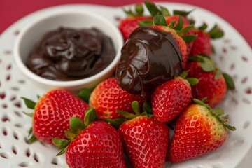 Wall Mural - Ripe Strawberries on a Heart-Shaped Plate with Chocolate Dipping Sauce in a Bowl on a Red Background