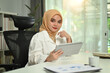 © Prathankarnpap - Portrait of modern asian muslim woman wearing hijab using digital tablet while sitting at her office
