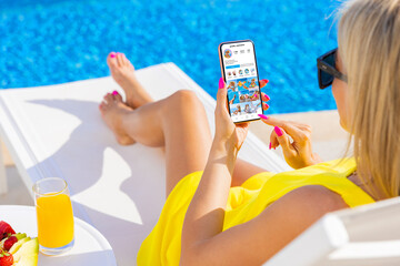 Wall Mural - Woman viewing social media app on mobile phone while relaxing by the pool
