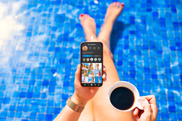 Wall Mural - Woman viewing social media app on mobile phone by the pool