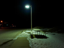 Table And Benches On Snow At Sidewalk By Illuminated Street Light During Night In City