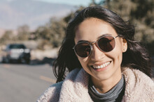 Close-up Portrait Of Smiling Young Woman Wearing Sunglasses On Road