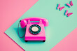 Spring creative layout with pink retro phone with colorful butterflies on pastel pink background and green grass. 80s or 90s retro fashion aesthetic telephone concept. Minimal romantic handset idea.