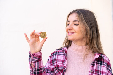 Wall Mural - Young pretty Romanian woman holding a Bitcoin at outdoors with happy expression