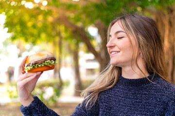 Wall Mural - Young pretty Romanian woman holding a burger at outdoors with happy expression