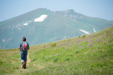 A tourist goes hiking in the mountains. Summer time of the year.