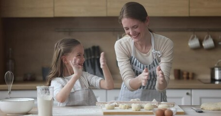 Wall Mural - Cheerful excited mom and daughter baking together, having fun in home kitchen, clapping floury hands, laughing at table with flour, dough, bakery food ingredients, enjoying leisure, hobby