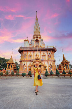 travel by asia. young woman in hat and yellow dress walking near the chalong buddhist temple on phuk