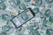 Banknot polski na wyświetlaczu telefonu komórkowego na tle gotówki 