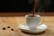 © vigenmnoyan - Coffee pouring into a cup on a wooden table. Black background.