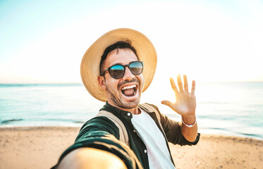 Wall Mural - Handsome young man taking selfie with smart mobile phone device at the beach - Happy tourist taking selfie on summer vacation - Smiling guy having fun outdoors - Life style and technology concept