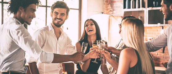 Wall Mural - Group of excited young people cheering with champagne while having home party