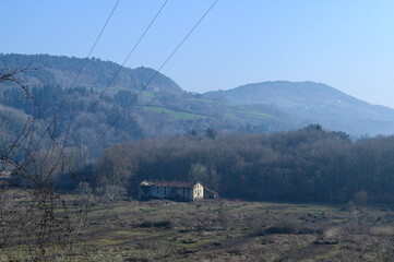 Wall Mural - landscape of an old ruined farmhouse in the Basque country, on a misty winter morning in the plain, in the background the green hills, above the blue sky,