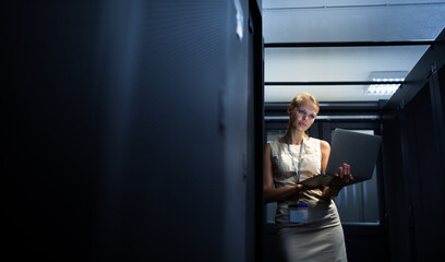 IT engineer standing before working server rack doing routine maintenance check and diagnostics using laptop