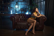 Sensual woman in sexy lingerie with yellow laces sitting on leather sofa