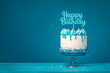 White happy birthday drip cake with teal ganache over blue background