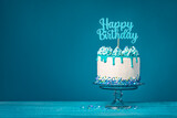 Fototapeta Tęcza - White happy birthday drip cake with teal ganache over blue background