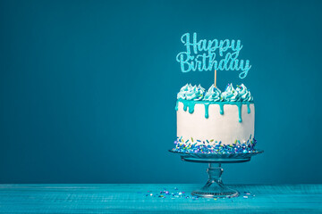 White happy birthday drip cake with teal ganache over blue background