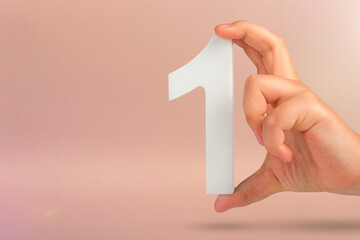 Fototapete - Number one in hand. A hand holds a white number one on a red background with copy space. Concept with number one. 1 percent rate, birthday, first or winner.