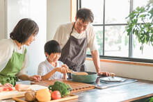 家のキッチンで子供と一緒に料理・クッキングする夫婦・親子・家族（味見）
