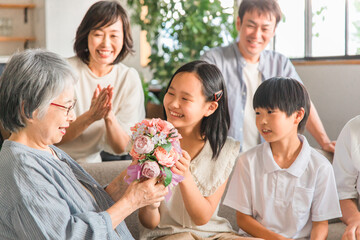 Wall Mural - 家のソファで孫から花束をもらう高齢者女性（三世代家族・ファミリー・家族団欒）
