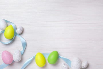 Wall Mural - Flat lay composition with festively decorated Easter eggs on white wooden background. Space for text