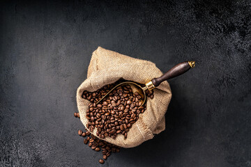 Wall Mural - Scoop of coffee beans in a bag on dark background. Top view of coffee. Copy space for text.