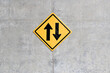 up and down arrows on yellow square diamond  traffic sign hanging on gray raw concrete wall, arrow indicates path that car can run in opposite direction, two way traffic sign