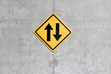 Up And Down Arrows On Yellow Square Diamond  Traffic Sign Hanging On Gray Raw Concrete Wall, Arrow Indicates Path That Car Can Run In Opposite Direction, Two Way Traffic Sign