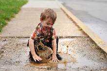 Playful Boy Playing In Puddle On Footpath