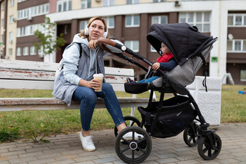 happy young woman parent with her little son in a stroller walks in the park and relaxes with coffee