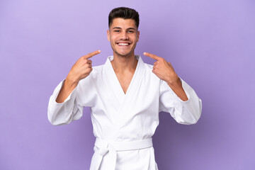 Wall Mural - Young caucasian man doing karate isolated on purple background giving a thumbs up gesture