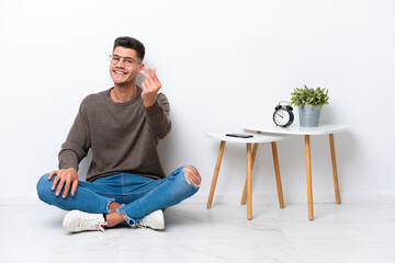 Wall Mural - Young caucasian man sitting in his home isolated on white background making money gesture