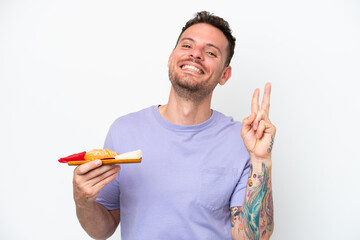 Wall Mural - Young caucasian man holding sashimi isolated on white background smiling and showing victory sign