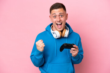 Wall Mural - Young brazilian man playing with a video game controller isolated on pink background celebrating a victory in winner position