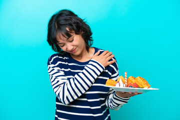 Wall Mural - Young Argentinian woman holding waffles isolated on blue background suffering from pain in shoulder for having made an effort