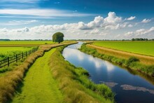 Dutch Polder And Water Area With Green Meadow In The Summer Countryside, Beneath A Blue Sky. Along The Road In The Countryside Of Noord Holland, The Netherlands, A Little Canal Or Ditch Can Be Seen