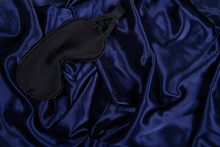 Black Silk Sleep Mask Lie On Dark Blue Silken Background With Copy Space. Flat Lay