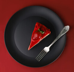 a piece of delicious sweet beautiful bright cake with strawberries on a black kitchen plate and a red background and decorated with pink berries around