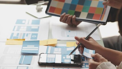 Close up ux developer and ui designer brainstorming about mobile app interface wireframe design on table with customer breif and color code at modern office.Creative digital development agency